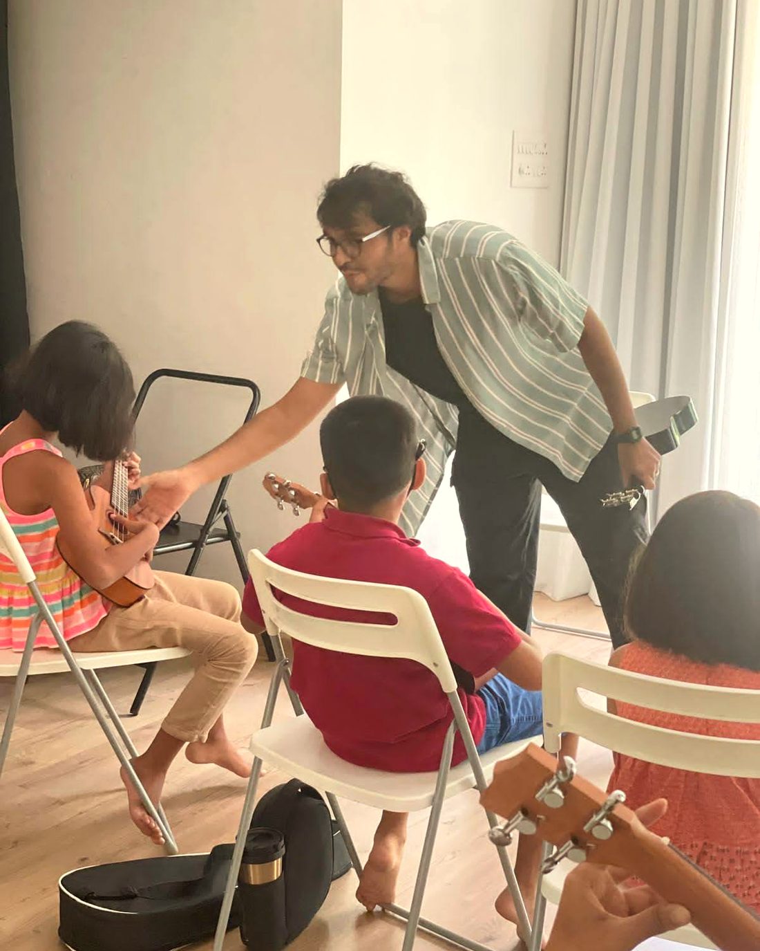 Akshit Deshmukh teaching a small group of children to play guitar in a sunlit room in Pune